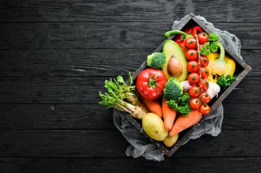 Tahta bir kutuda sebzeler. Avokado, salatalık, soğan, sarımsak, domates, havuç, yabanturpu. Üst te. Metniniz için boş alan.