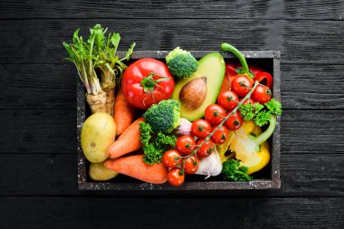 Tahta bir kutuda sebzeler. Avokado, salatalık, soğan, sarımsak, domates, havuç, yabanturpu. Üst te. Metniniz için boş alan.