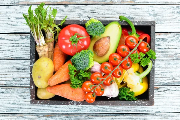 Tahta bir kutuda sebzeler. Avokado, salatalık, soğan, sarımsak, domates, havuç, yabanturpu. Üst te. Metniniz için boş alan.