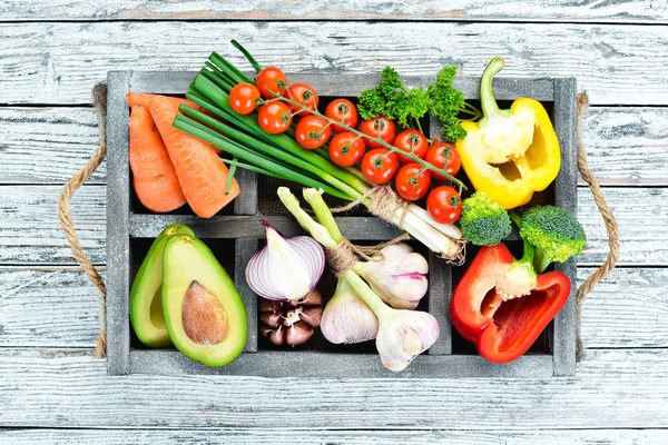 Tahta bir kutuda sebzeler. Avokado, salatalık, soğan, sarımsak, domates, havuç, yabanturpu. Üst te. Metniniz için boş alan.