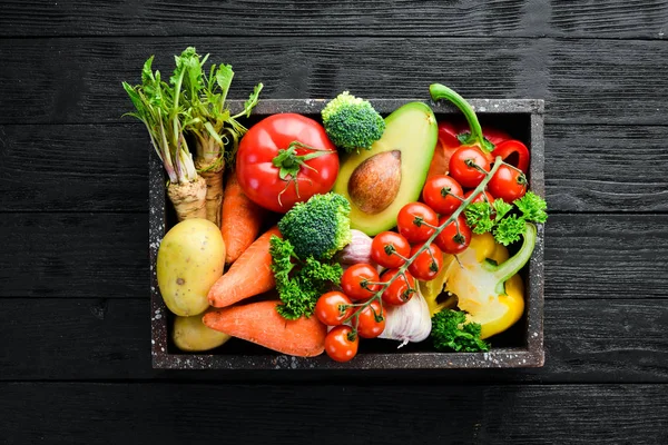 Tahta bir kutuda sebzeler. Avokado, salatalık, soğan, sarımsak, domates, havuç, yabanturpu. Üst te. Metniniz için boş alan.