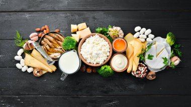 Doğal kalsiyum içeren ürünler: peynir, süt, parmesan, ekşi krema, balık, badem, maydanoz, sarımsak, brokoli. Siyah ahşap bir arka plan üzerinde. Üst te. Ücretsiz kopyalama alanı.