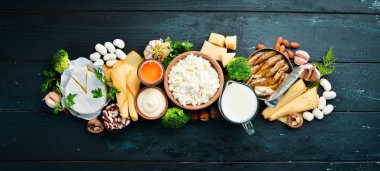 Doğal kalsiyum içeren ürünler: peynir, süt, parmesan, ekşi krema, balık, badem, maydanoz, sarımsak, brokoli. Siyah ahşap bir arka plan üzerinde. Üst te. Ücretsiz kopyalama alanı.