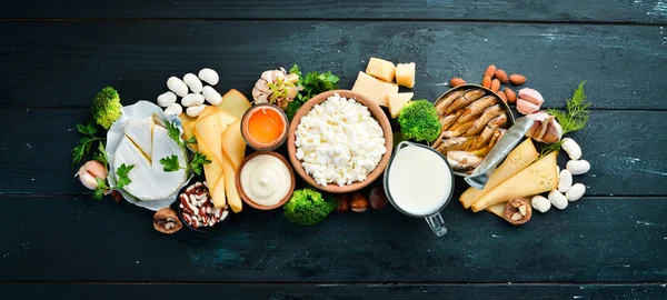 Doğal kalsiyum içeren ürünler: peynir, süt, parmesan, ekşi krema, balık, badem, maydanoz, sarımsak, brokoli. Siyah ahşap bir arka plan üzerinde. Üst te. Ücretsiz kopyalama alanı.