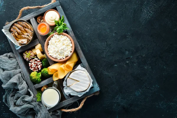 Doğal kalsiyum içeren ürünler: peynir, süt, parmesan, ekşi krema, balık, badem, maydanoz, sarımsak, brokoli. Siyah ahşap bir arka plan üzerinde. Üst te. Ücretsiz kopyalama alanı.