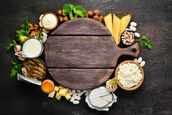 Kalsiyum açısından zengin ürün grubu. Sağlıklı diyet gıda: peynir, süt, parmesan, ekşi krema, balık, badem, maydanoz, sarımsak, brokoli. Eski arka planda. Üst te. Ücretsiz kopyalama alanı.