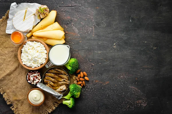 Kalsiyum açısından zengin ürün grubu. Sağlıklı diyet gıda: peynir, süt, parmesan, ekşi krema, balık, badem, maydanoz, sarımsak, brokoli. Eski arka planda. Üst te. Ücretsiz kopyalama alanı.