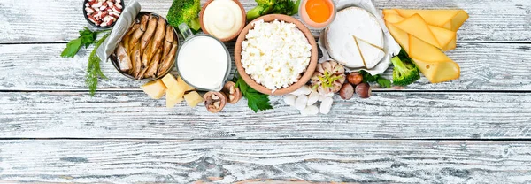 Food with calcium. A variety of foods rich in calcium: cheese, milk, parmesan, sour cream, fish, almonds, parsley, garlic, broccoli. On a white wooden background. Top view. Free copy space.