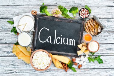 Kalsiyumlu yiyecekler. Kalsiyum açısından zengin gıdalar çeşitli: peynir, süt, parmesan, ekşi krema, balık, badem, maydanoz, sarımsak, brokoli. Beyaz ahşap bir arka plan üzerinde. Üst te. Ücretsiz kopyalama alanı.