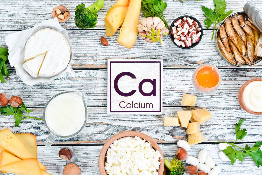 Food with calcium. A variety of foods rich in calcium: cheese, milk, parmesan, sour cream, fish, almonds, parsley, garlic, broccoli. On a white wooden background. Top view. Free copy space.