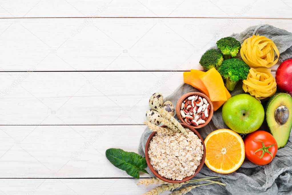 Healthy food containing carbohydrates: bread, pasta, avocados, flour, pumpkin, broccoli, beans, spinach. On a white background. Top view. Free copy space.