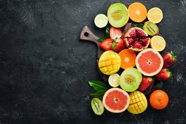 Siyah bir arka plan üzerinde taze tropikal meyveler. Narenciye, kavun, nar, çilek, muz. Üst te. Metniniz için boş alan.