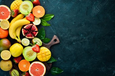 Siyah bir arka plan üzerinde taze tropikal meyveler. Narenciye, kavun, nar, çilek, muz. Üst te. Metniniz için boş alan.