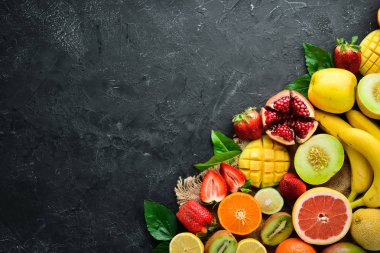 Siyah bir arka plan üzerinde taze tropikal meyveler. Narenciye, kavun, nar, çilek, muz. Üst te. Metniniz için boş alan.