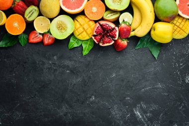 Siyah bir arka plan üzerinde taze tropikal meyveler. Narenciye, kavun, nar, çilek, muz. Üst te. Metniniz için boş alan.