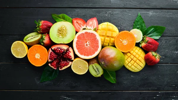 Fresh tropical fruits on a black background. Citrus, melon, pomegranate, strawberry, banana. Top view. Free space for your text.