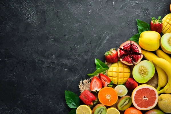 Siyah bir arka plan üzerinde taze tropikal meyveler. Narenciye, kavun, nar, çilek, muz. Üst te. Metniniz için boş alan.