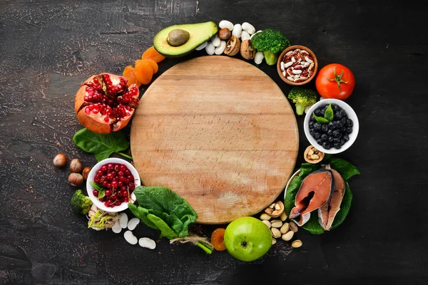 Healthy food for the heart: Fish, blueberries, nuts, pomegranate, avocados, tomatoes, spinach, flax. On a dark background. Top view. Free space for your text.