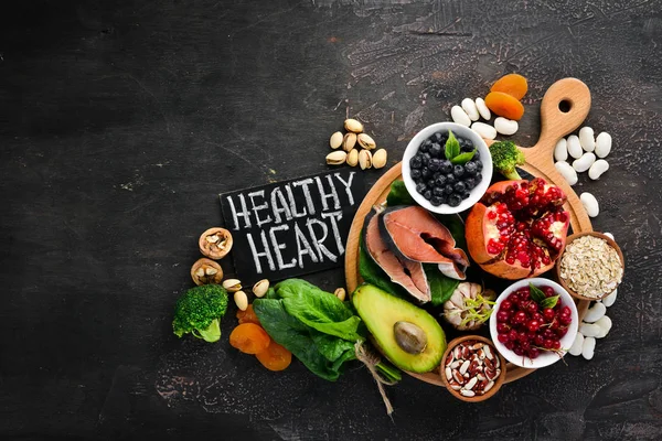Healthy food for the heart: Fish, blueberries, nuts, pomegranate, avocados, tomatoes, spinach, flax. On a dark background. Top view. Free space for your text.