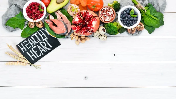 Healthy food for the heart: Fish, blueberries, nuts, pomegranate, avocados, tomatoes, spinach, flax. On a white wooden background. Top view.