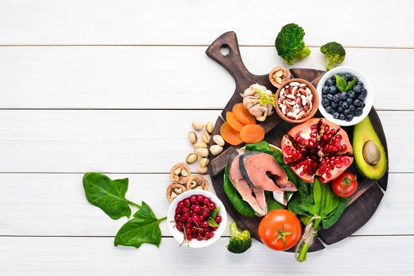 Healthy food for the heart: Fish, blueberries, nuts, pomegranate, avocados, tomatoes, spinach, flax. On a white wooden background. Top view.
