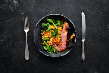 Sebzeli deniz ürünleri. Karides ve midye ile haşlanmış sebze. Siyah bir tabakta. Üst te. Ücretsiz kopyalama alanı.