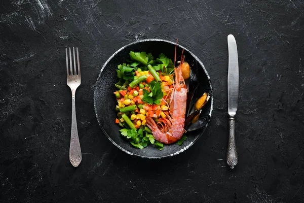 Seafood with vegetables. Boiled vegetables with shrimp and mussels. In a black plate. Top view. Free copy space.