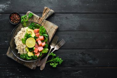 Somon, avokado ve ıspanaklı pilav. Ahşap arka plan üst görünümünde siyah bir tabak ta. Metniniz için boş alan. Düz yatıyordu
