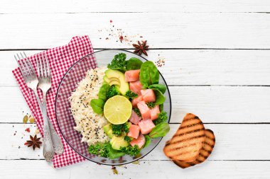 Somon, avokado ve ıspanaklı pilav. Ahşap arka plan üst görünümünde siyah bir tabak ta. Metniniz için boş alan. Düz yatıyordu