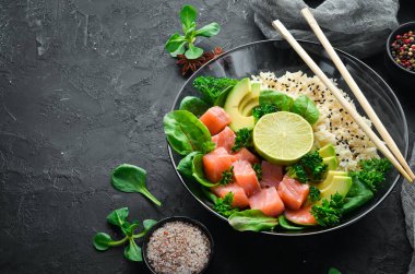 Somon, avokado ve ıspanaklı pilav. Ahşap arka plan üst görünümünde siyah bir tabak ta. Metniniz için boş alan. Düz yatıyordu