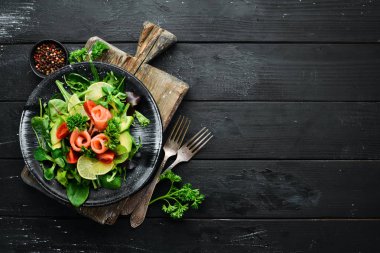 Somon, avokado, domates ve ıspanak salatası. Ahşap arka plan üst görünümünde siyah bir tabak ta. Metniniz için boş alan. Düz yatıyordu