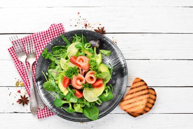 Somon, avokado, domates ve ıspanak salatası. Ahşap arka plan üst görünümünde siyah bir tabak ta. Metniniz için boş alan. Düz yatıyordu