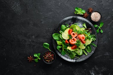 Somon, avokado, domates ve ıspanak salatası. Ahşap arka plan üst görünümünde siyah bir tabak ta. Metniniz için boş alan. Düz yatıyordu