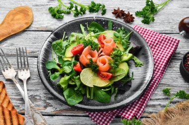 Somon, avokado, domates ve ıspanak salatası. Ahşap arka plan üst görünümünde siyah bir tabak ta. Metniniz için boş alan. Düz yatıyordu