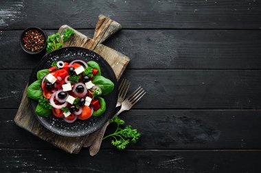 Domates, kırmızı biber, soğan ve beyaz peynir ile Yunan salatası. Ahşap arka plan üst görünümünde siyah bir tabak ta. Metniniz için boş alan. Düz yatıyordu