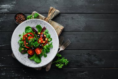 Ispanak, domates, kırmızı biber ve kabak çekirdeği ile sebze salatası ahşap bir arka plan üst görünümü üzerinde bir tabakta. Metniniz için boş alan. Düz yatıyordu