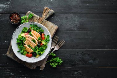 Tavuk fileto, zeytin, domates ve avokado ile salata ahşap bir arka plan üst görünümü üzerinde bir tabakta. Metniniz için boş alan. Düz yatıyordu