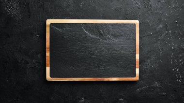 Taş mutfak tahtası. Siyah taş arka plan üzerine afiş. Üst te. Metniniz için boş alan.