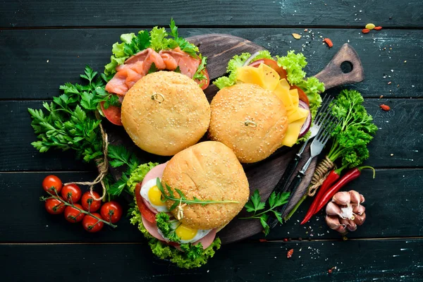 Set of burgers with meat, cheese, fish and vegetables. On a black background. Top view. Free space for your text.