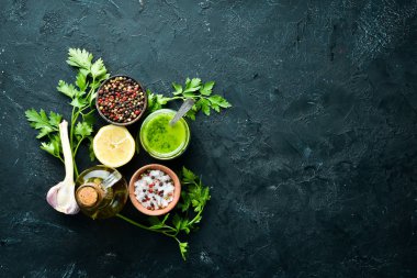 Yeşil maydanoz sosu, zeytinyağı ve baharatlar. Chimichurri sosu için malzemeler. Siyah bir arka plan üzerinde. Üst te. metniniz için boş alan.
