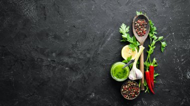 Green parsley sauce, olive oil and spices. Ingredients for chimichurri sauce. On a black background. Top view. free space for your text. clipart
