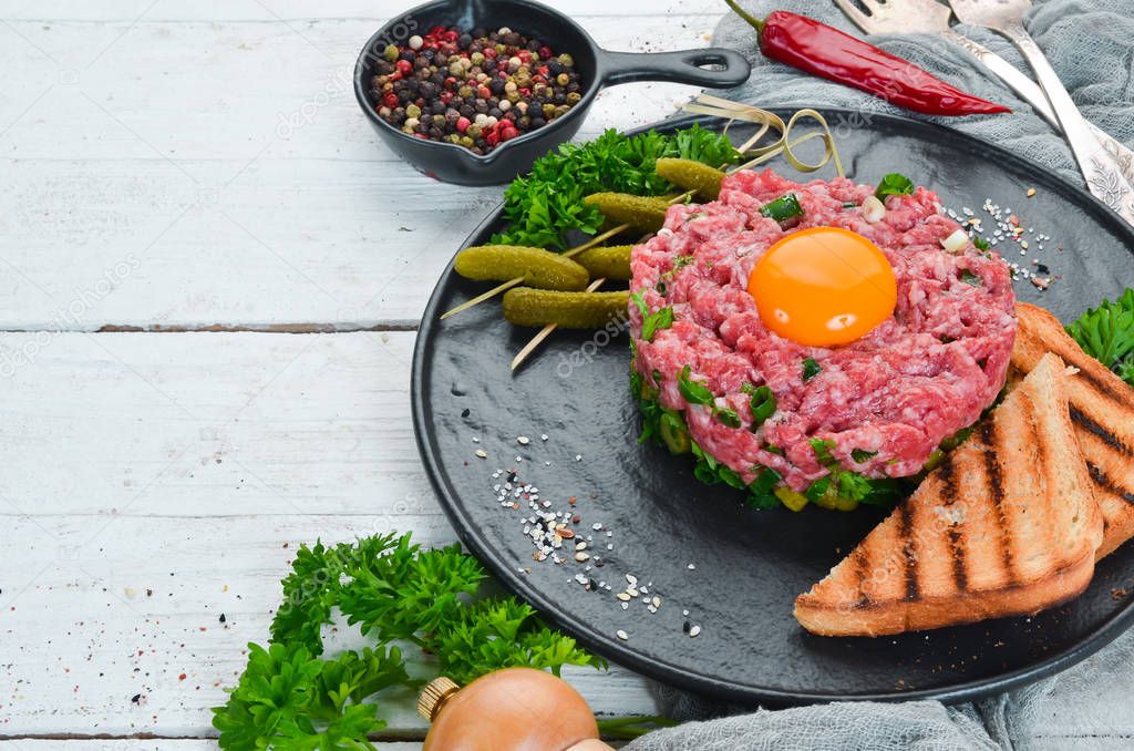 Beef steak tartare with raw egg yolk, pickled cucumber and onions. French cuisine. Top view. Free space for your text.