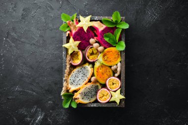 Tropikal meyve - siyah bir arka plan üzerinde tutku meyve, ananas, ejderha meyve, kivi ve kaktüs. Üst te. Metin için boş alan.