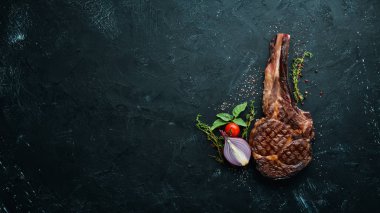 Izgara kovboy et biftek, otlar ve baharatlar siyah taş arka plan üzerinde. Barbekü. Üst te. Metin için boş alan.