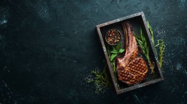 Izgara kovboy et biftek, otlar ve baharatlar siyah taş arka plan üzerinde. Barbekü. Üst te. Metin için boş alan.
