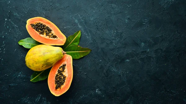 Fresh papaya on a black stone background. Tropical Fruits. Top view. Free space for text.