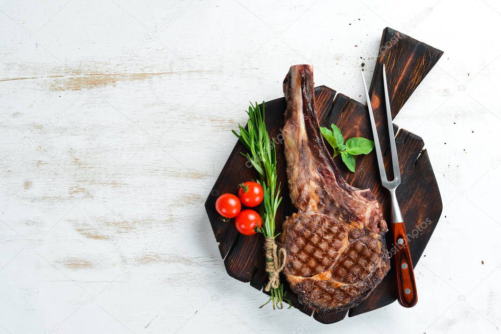 Grilled steak on a bone on a white wooden background. Barbecue. Top view. Free space for text.
