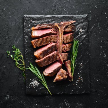 Beef T-Bone steak on a black table. Top view. Free space for text. clipart