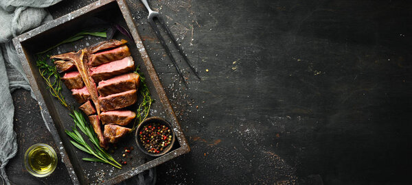 Beef T-Bone steak on a black table. Top view. Free space for text.
