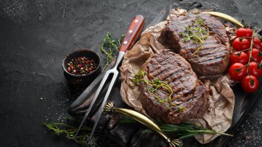 Izgara ribeye sığır eti biftek, otlar ve baharatlar karanlık bir masada. Üst te. Metniniz için boş alan.